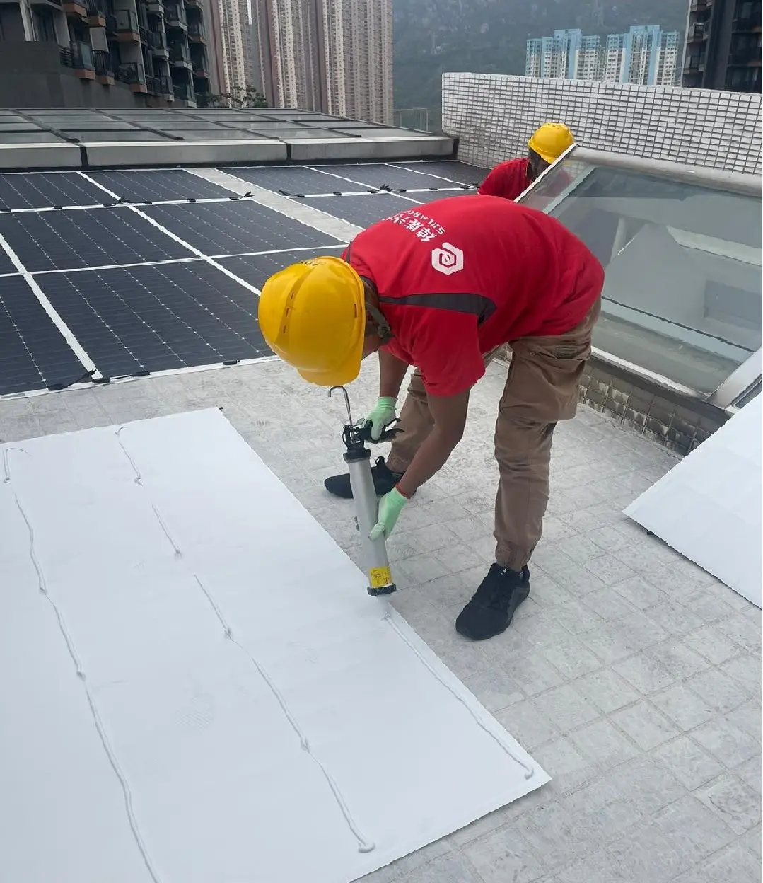 身穿紅色綽能光伏工作服及安全帽的人員在屋頂進行密封施工。
