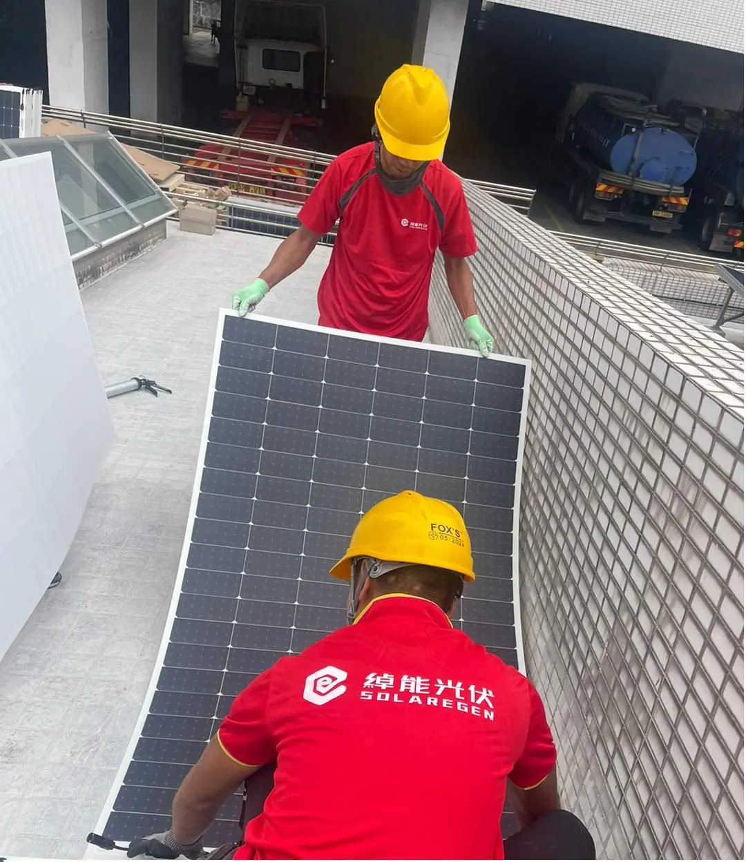 兩位身穿紅色綽能光伏工作服及安全帽的人員在屋頂搬運太陽能板。